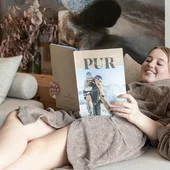 Drei Kinder in braunen Bademänteln lesen zusammen ein Magazin auf dem Sofa