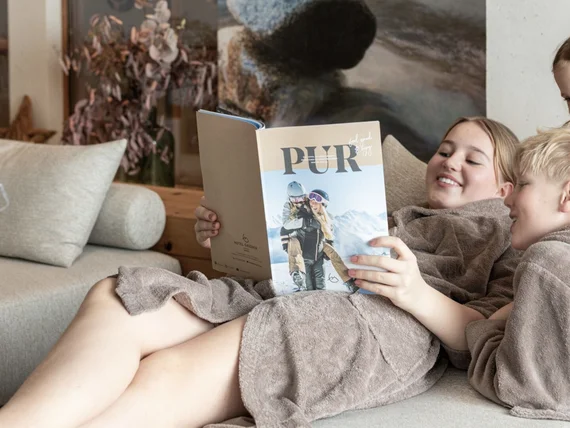 Drei Kinder in braunen Bademänteln lesen zusammen ein Magazin auf dem Sofa
