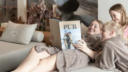 Drei Kinder in braunen Bademänteln lesen zusammen ein Magazin auf dem Sofa