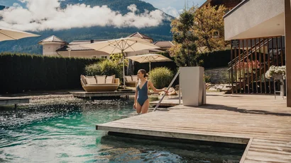 Frau im Badeanzug steigt in einen Pool mit Bergblick und Sonnenschirmen