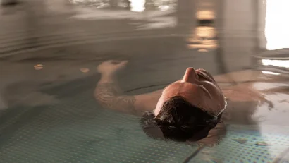 Person entspannt schwebend im Wasser mit sichtbaren Tätowierungen am Arm