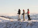 Drei Menschen mit Schneeschuhen auf verschneitem Berggipfel mit Bergpanorama