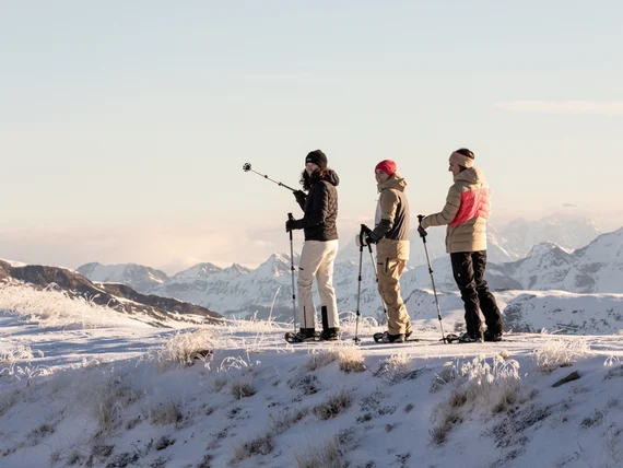 Drei Menschen mit Schneeschuhen auf verschneitem Berggipfel mit Bergpanorama