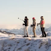 Drei Menschen mit Schneeschuhen auf verschneitem Berggipfel mit Bergpanorama