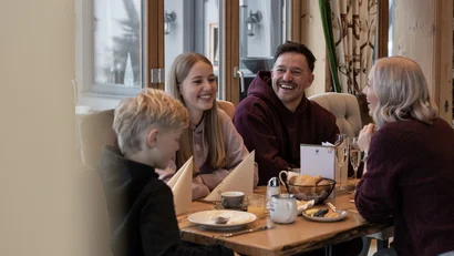 Vier Personen sitzen lachend an einem Tisch und frühstücken gemeinsam