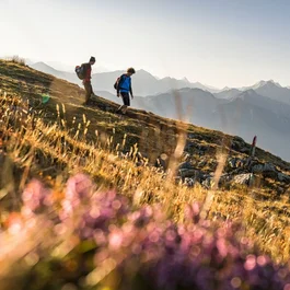 Zwei Wanderer auf einem Bergpfad mit Alpenpanorama im Hintergrund