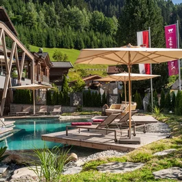 Hotelpool mit Liegestühlen und Sonnenschirmen in grüner Alpenlandschaft