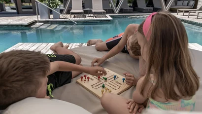 Drei Kinder sitzen auf auf einem großen Loungesessel vor dem Naturpool im Hotel Gassner und spielen ein Brettspiel