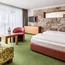Gemütliche, großzügige Suite mit Naturmaterialien, Doppelbett und gemütlicher Lounge mit Couch, Tisch und Sitzgelegenheit und gepackter Wellnesstasche