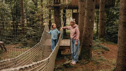 Kind und Frau auf einem Seilnetz im Wald beim Klettern