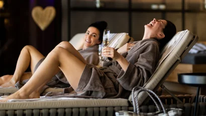 Zwei Frauen in Bademänteln entspannen auf Liegestühlen mit einem Glas Sekt