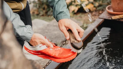 Person reinigt rote Sportschuhe mit Bürste an Wasserstelle im Freien