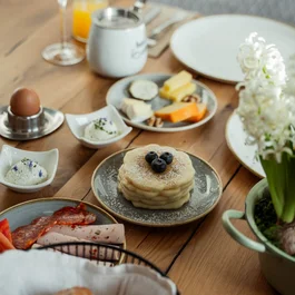 Frühstückstisch mit Pfannkuchen, Kaffee, Ei, Käse, Aufschnitt und Blumen