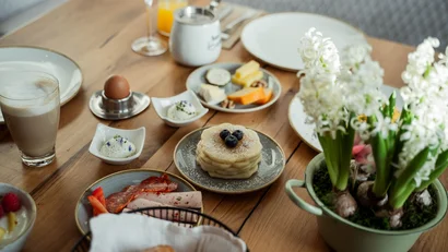 Frühstückstisch mit Pfannkuchen, Kaffee, Ei, Käse, Aufschnitt und Blumen