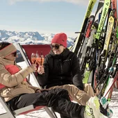Zwei Frauen stoßen mit Getränken auf einer sonnigen Skipause an