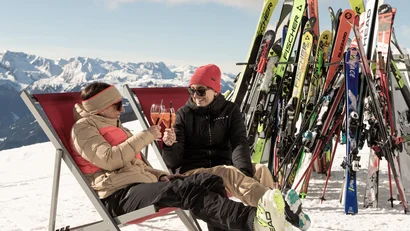 Zwei Frauen stoßen mit Getränken auf einer sonnigen Skipause an