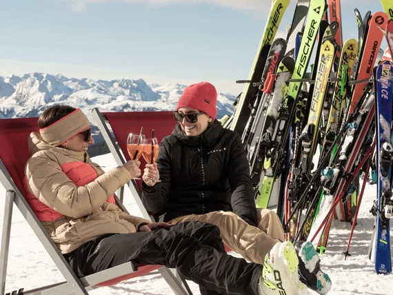 Zwei Frauen stoßen mit Getränken auf einer sonnigen Skipause an